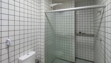 A small, tiled bathroom with a shower, toilet, and a shelf with toiletries.
