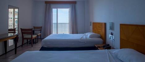 Habitación de hotel con dos camas, un escritorio, sillas, un ventanal con vistas y un cabecero de madera.