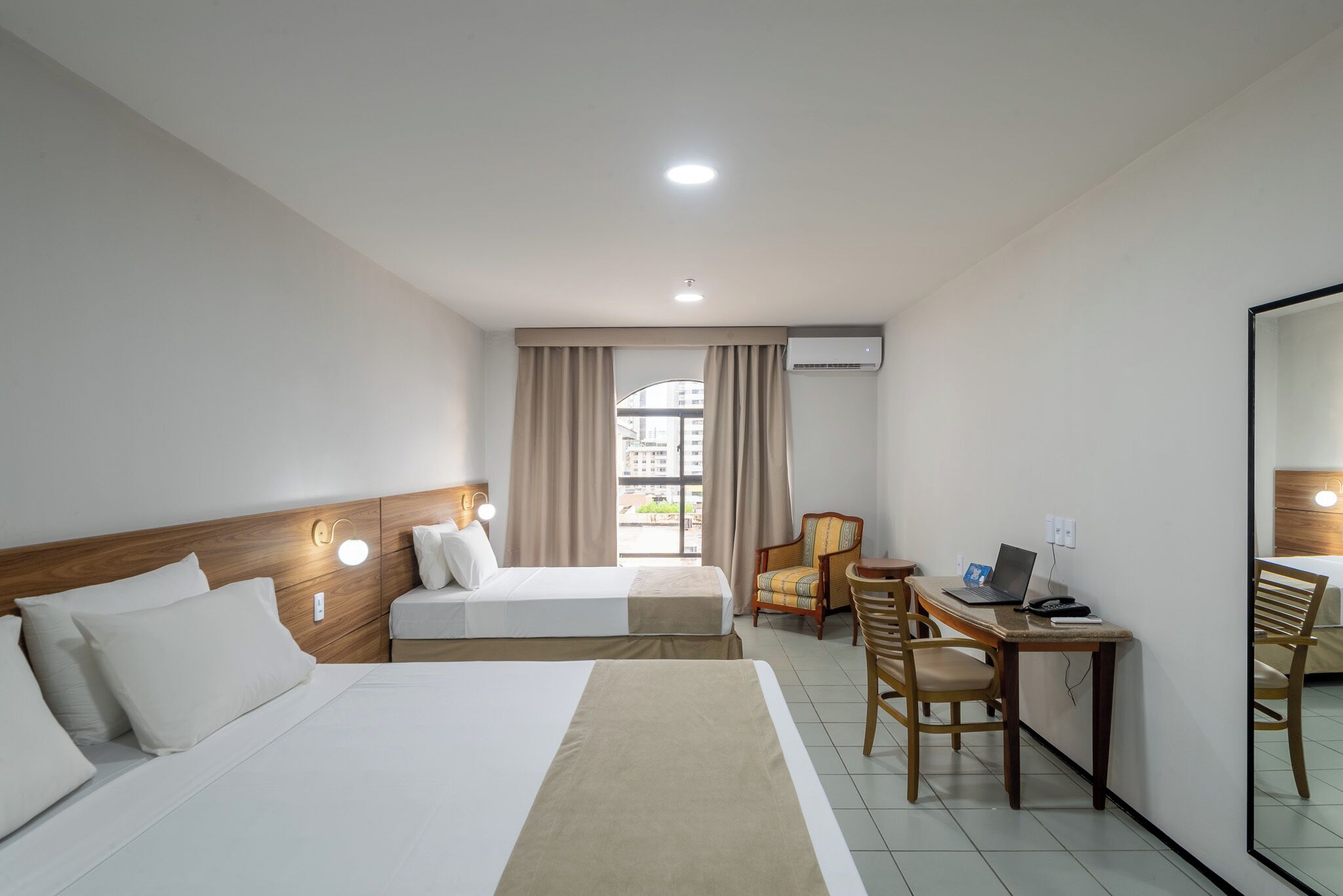 A hotel room with two beds, a desk with a laptop, a chair, and a large mirror.