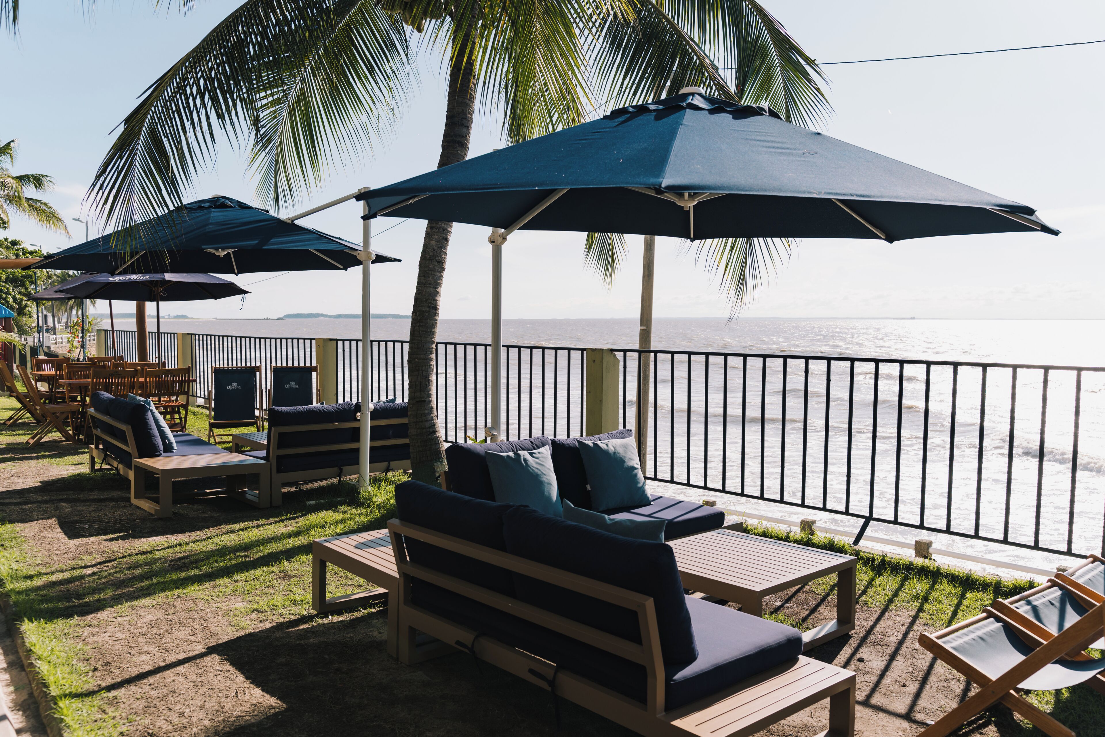 A seaside patio with wooden lounge chairs and umbrellas, overlooking the ocean.