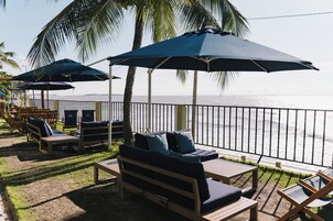 A seaside patio with wooden lounge chairs and umbrellas, overlooking the ocean.