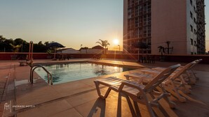 Zona de piscina con sillas de descanso y un edificio al fondo.