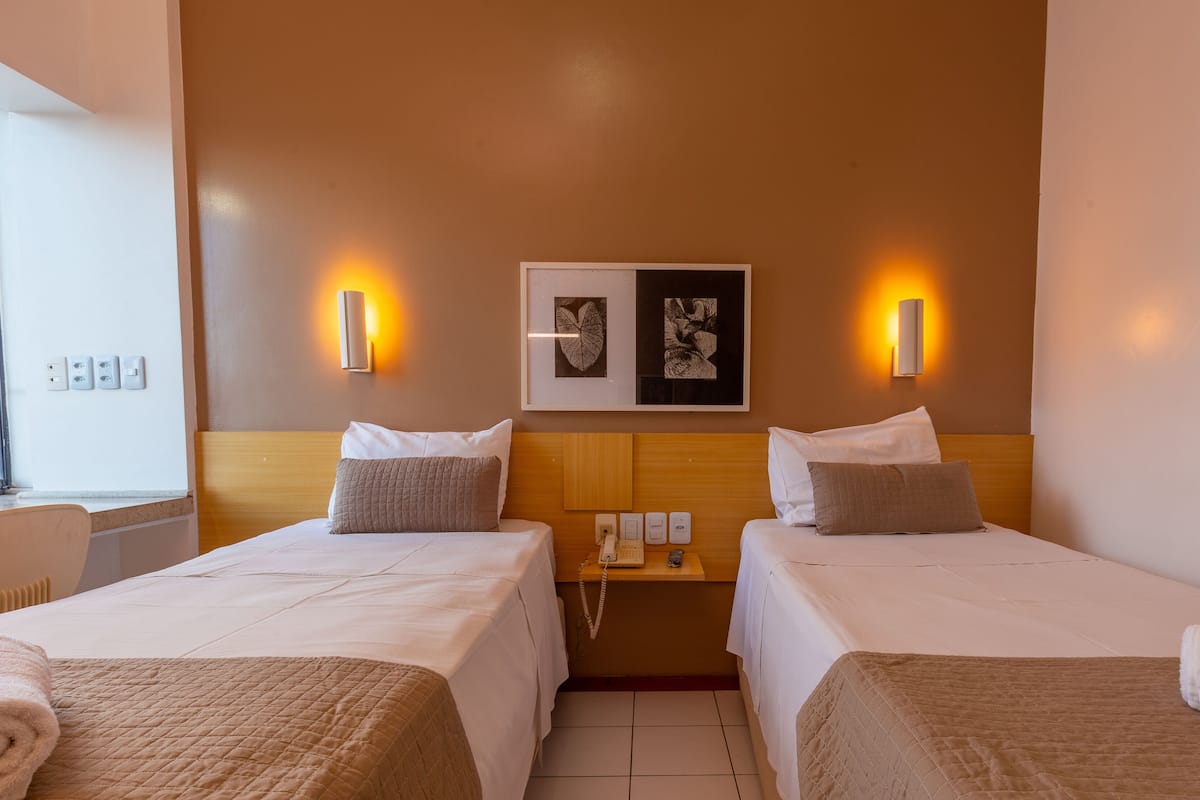 A hotel room with two beds, a wooden headboard, wall-mounted artwork, and bedside lamps.
