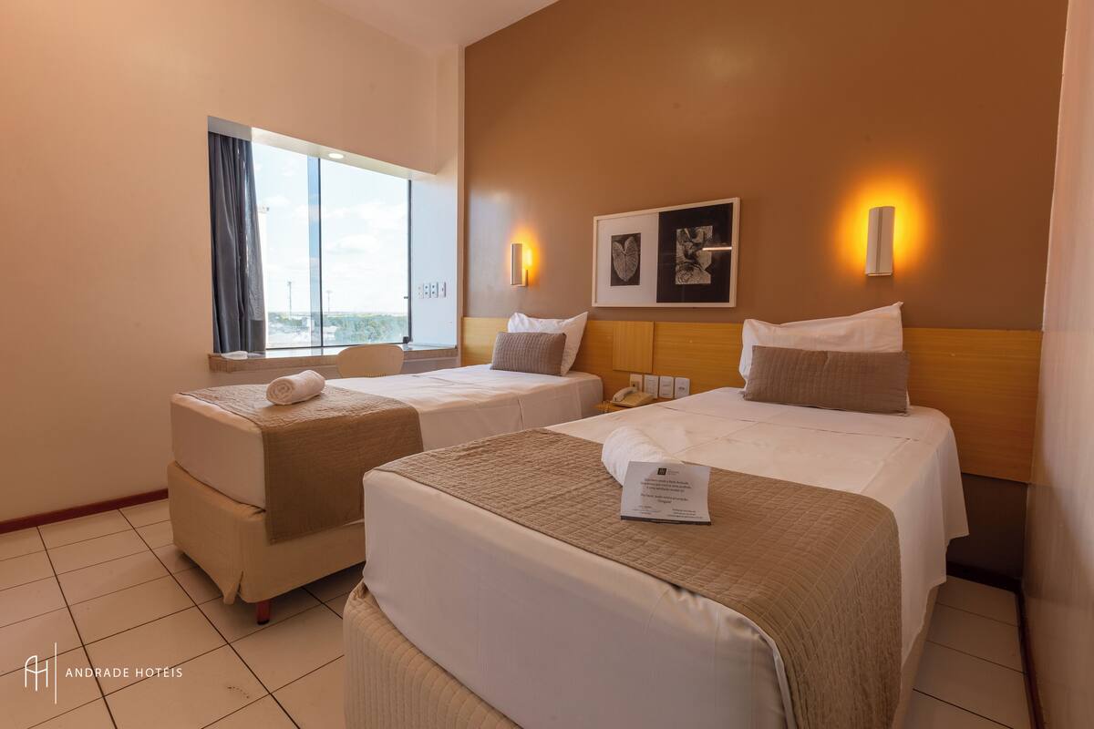 A hotel room with two beds, a large window, and artwork on the wall.