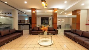 Un moderno vestíbulo de hotel con dos sofás de cuero marrón, una mesa de centro de vidrio con un centro de flores y un mostrador de recepción al fondo.