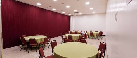 A conference room with round tables and red chairs, white walls, and a red curtain backdrop.