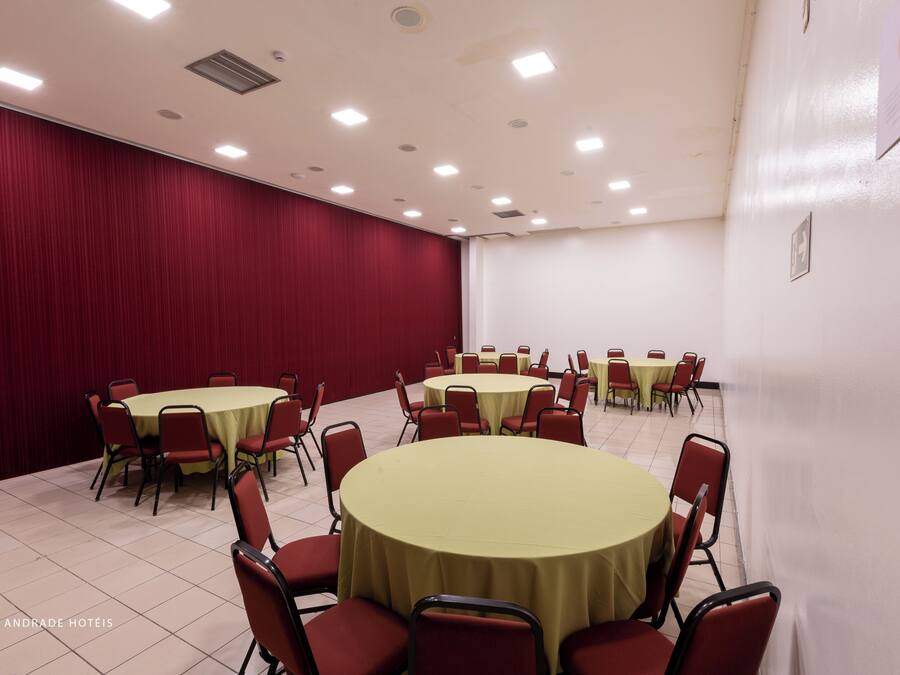 A conference room with round tables and red chairs, white walls, and a red curtain backdrop.