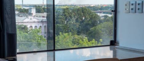 A hotel room with a large window, a bed, a chair, and a view of a cityscape.