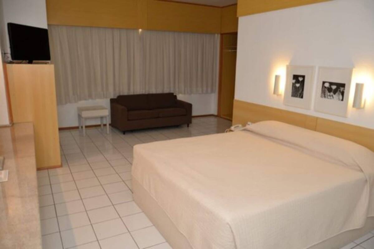A hotel room with a bed, a sofa, a television, and artwork on the wall.