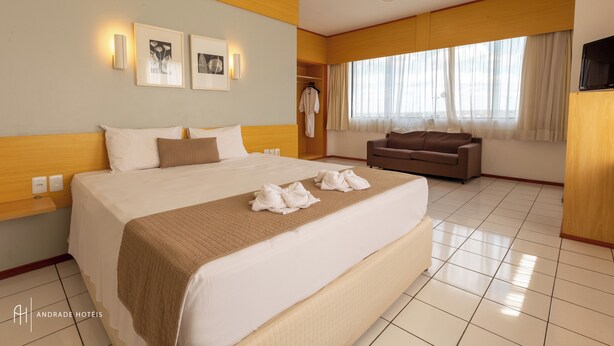 Una habitación de hotel con una cama grande, un sofá, un televisor y obras de arte en la pared.