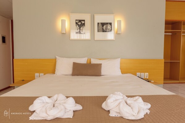 A hotel room with a large bed, two wall-mounted light fixtures, and two framed pictures above the bed.