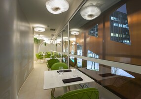 A modern dining area with glass walls, green chairs, and white tables.