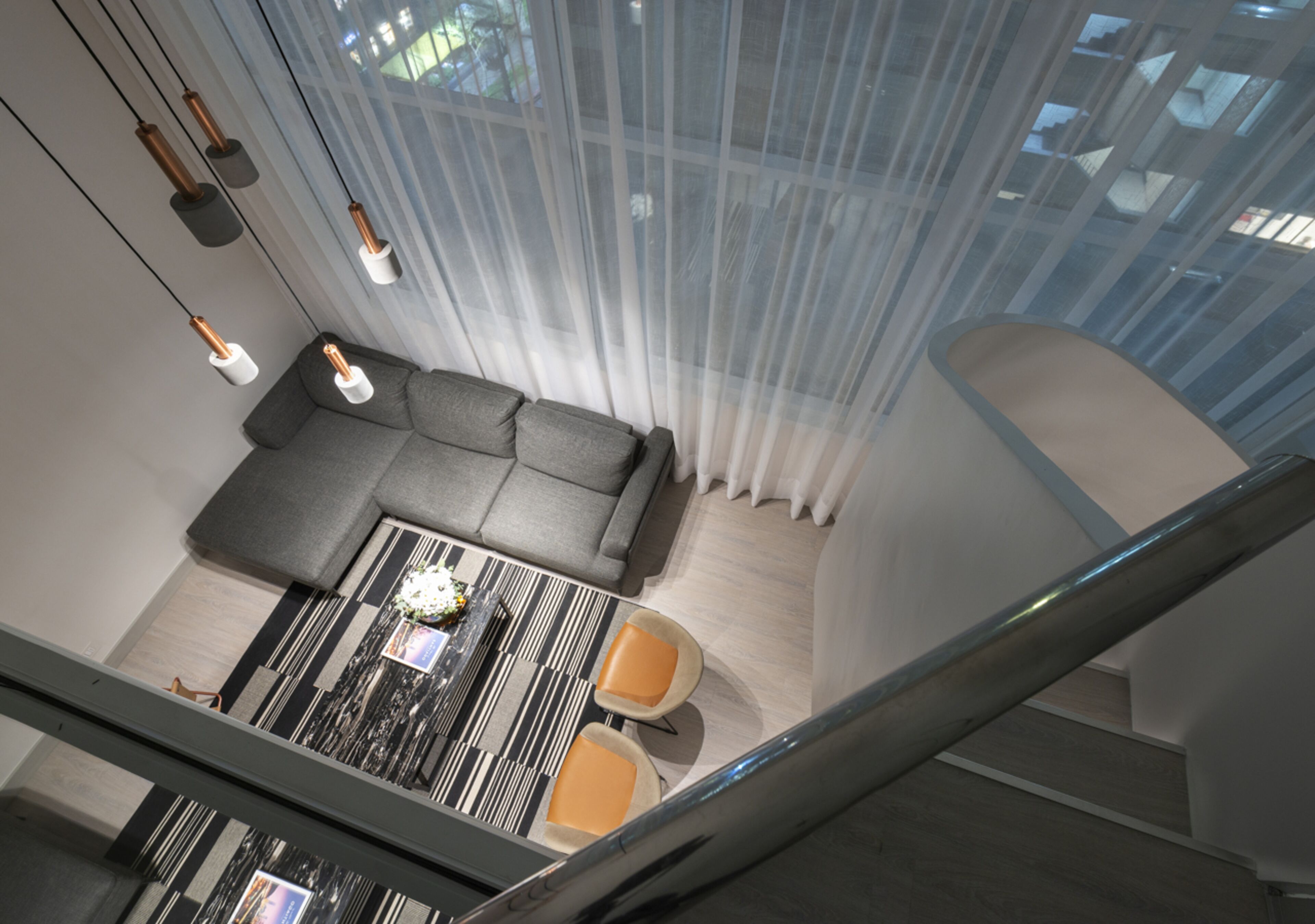 A modern living room with a sectional sofa, a dining table with chairs, and a staircase.