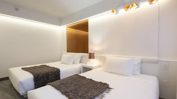 Habitación de hotel con dos camas, una mesita de noche con lámpara y una lámpara moderna sobre las camas.