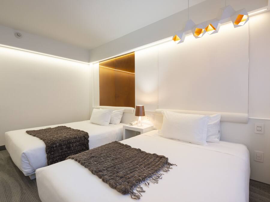 Habitación de hotel con dos camas, una mesita de noche con lámpara y una lámpara moderna sobre las camas.