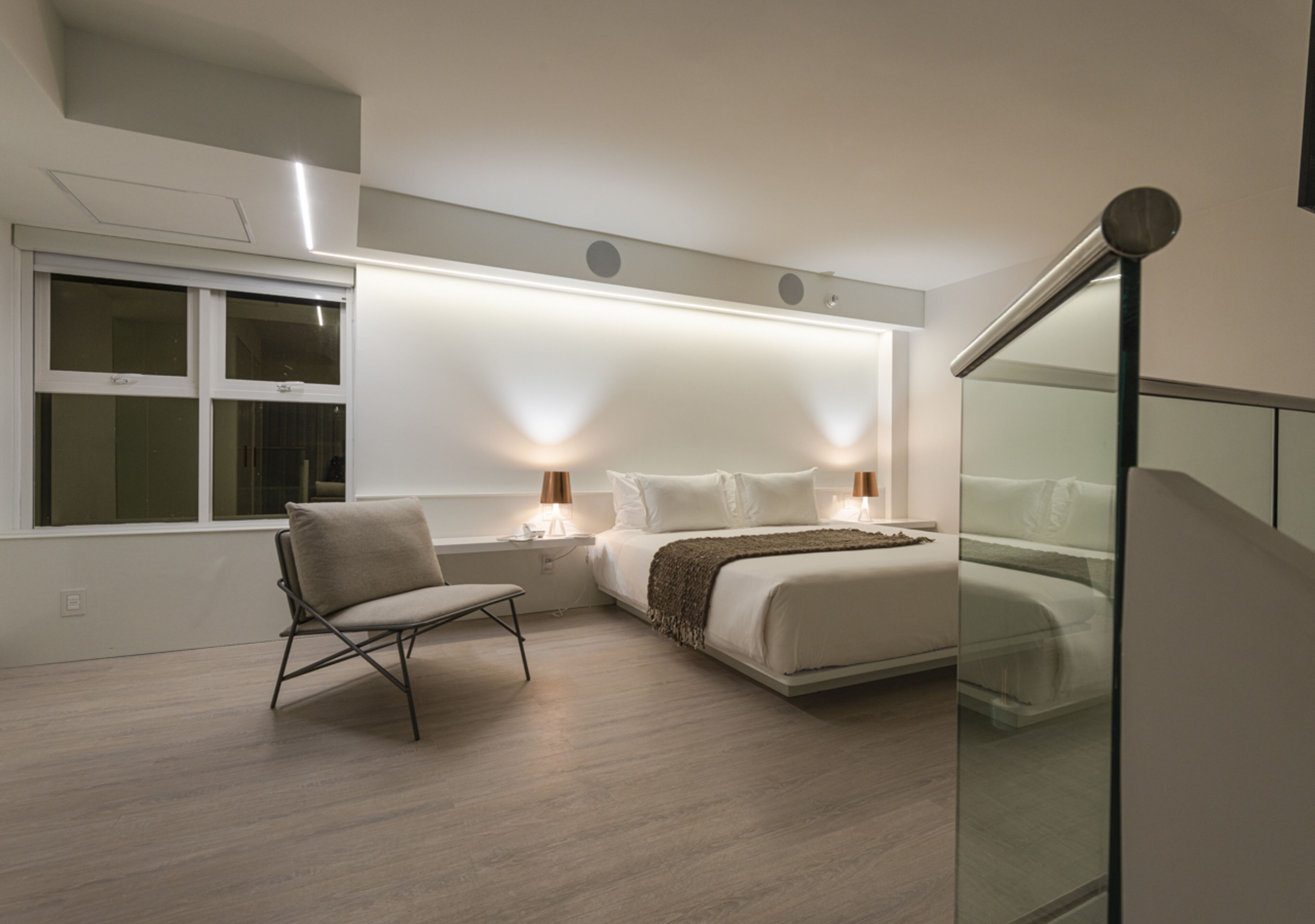 A modern bedroom with a bed, bedside tables, a chair, and a window.