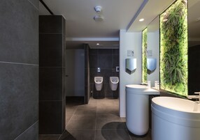 Un baño moderno con baldosas oscuras, un lavabo grande y un espejo montado en la pared.