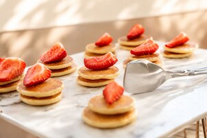 Una encimera de mármol con tortitas apiladas, fresas por encima y una espátula metálica.