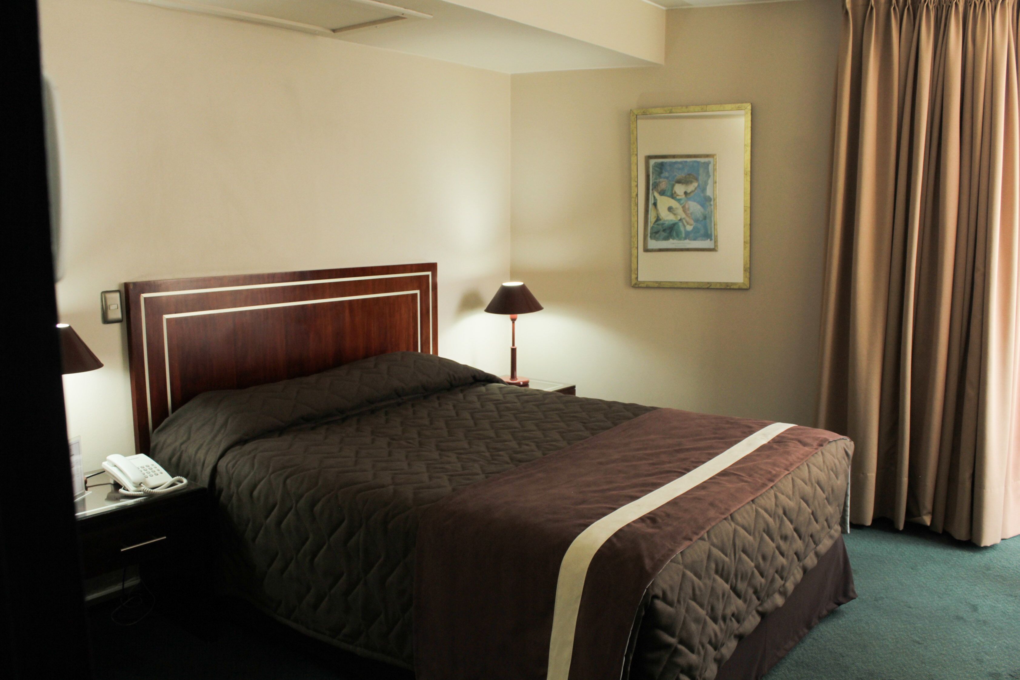 A neatly made bed with a quilted cover, a bedside lamp, and a telephone on the nightstand.