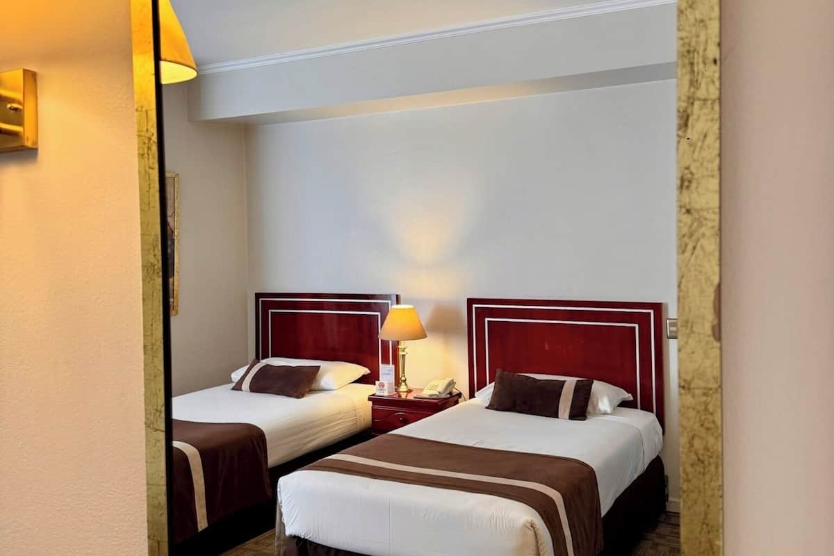 A hotel room with two beds, a nightstand with a lamp, and a mirror on the wall.