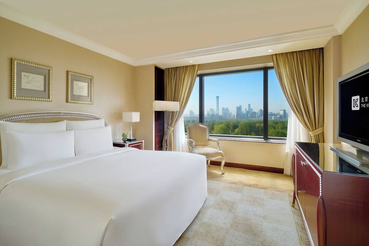 Habitación de hotel con una cama grande, televisor, una silla y vistas a un horizonte urbano.