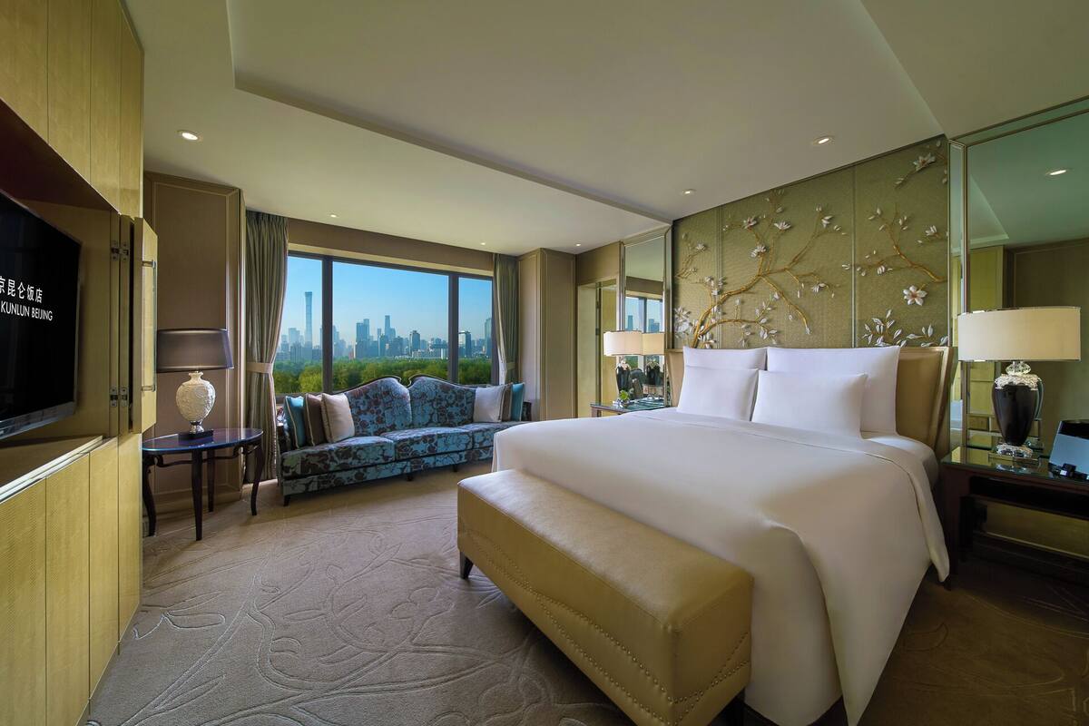 Una habitación de hotel con una cama grande, un sofá, televisión y vista a la ciudad.