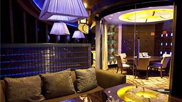 A modern lounge area with a curved wooden bench, a round table with a vase and candles, and ambient lighting.