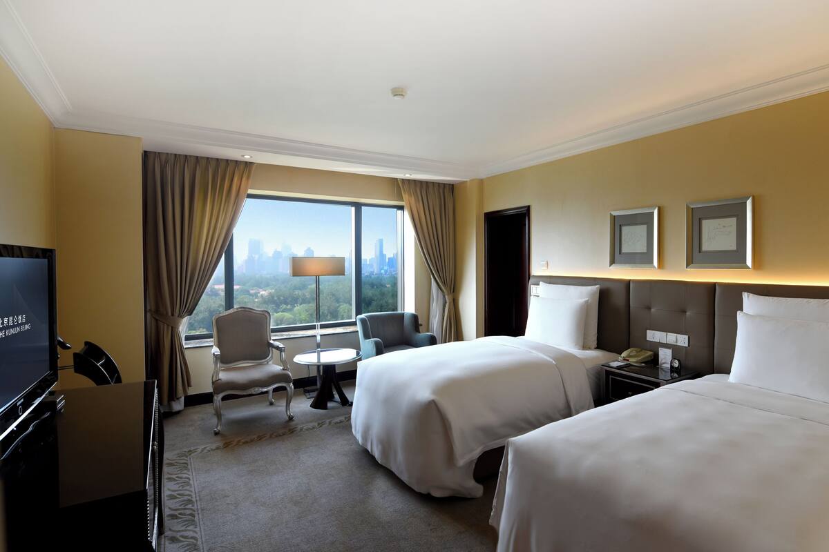 Habitación de hotel con dos camas, televisión, escritorio, silla, lámpara y vistas del horizonte urbano.