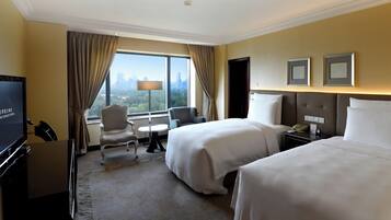 A hotel room with two beds, a TV, a desk, a chair, a lamp, and a view of the city skyline.