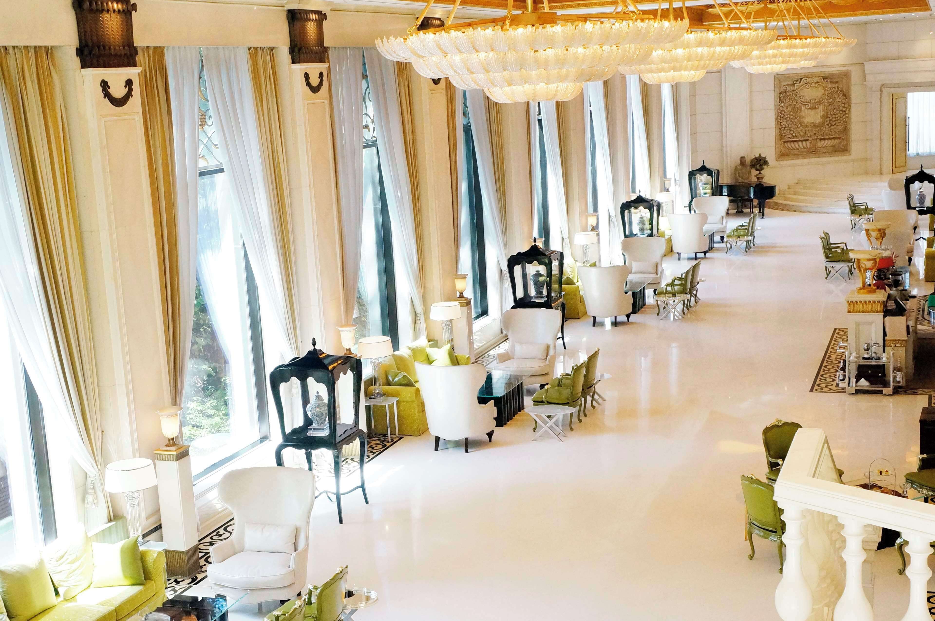 Un amplio vestíbulo de hotel con un largo pasillo flanqueado por zonas de estar, ventanas grandes y candelabros.