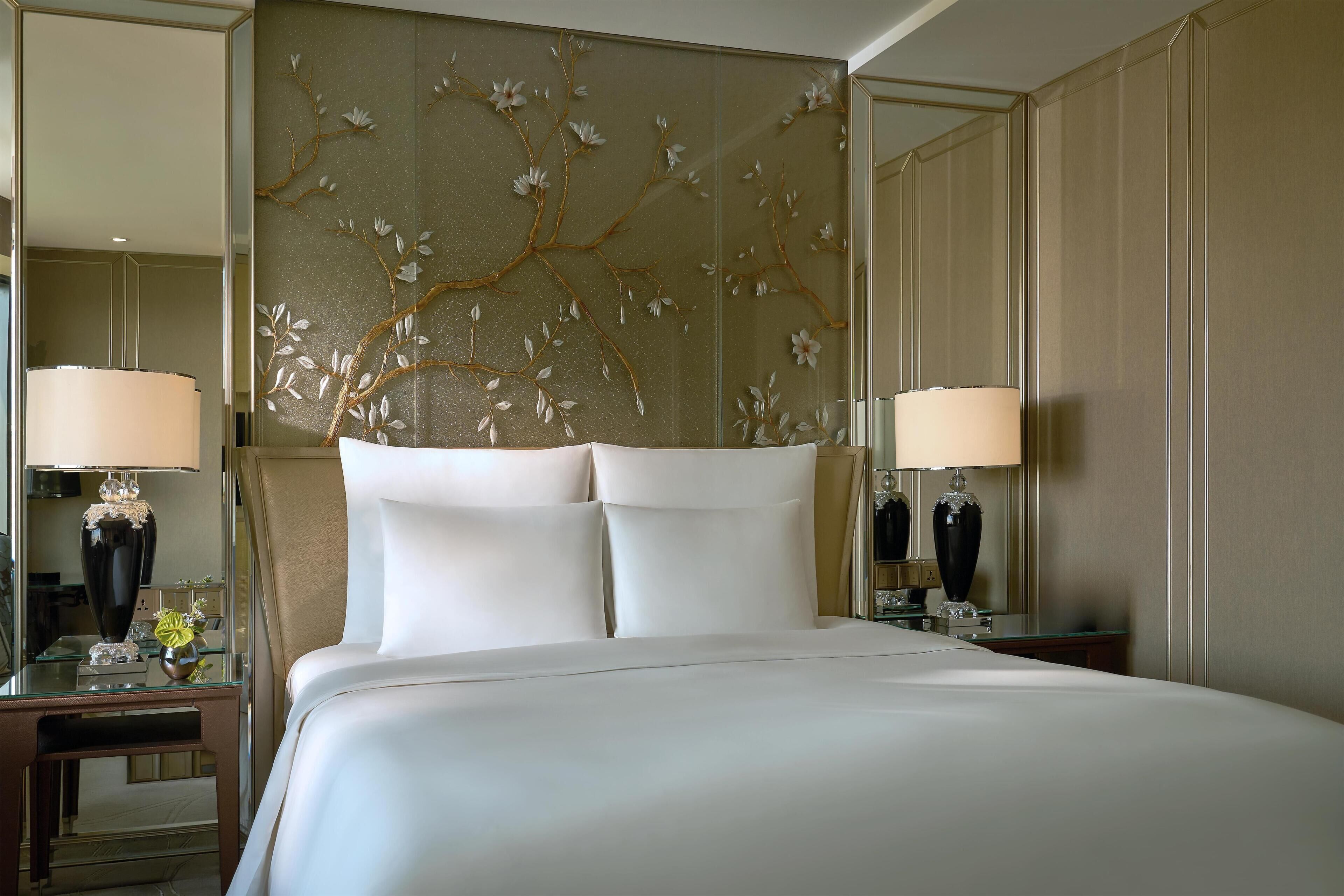 Une chambre d’hôtel avec un grand lit, deux tables de chevet avec des lampes, un panneau décoratif au mur et un miroir.