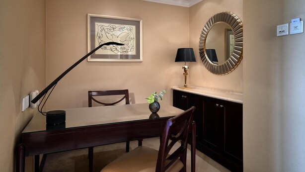 A dining area with a table, chairs, a lamp, a framed artwork, a mirror, and a vase with flowers. - The Kunlun Beijing (Beijing)