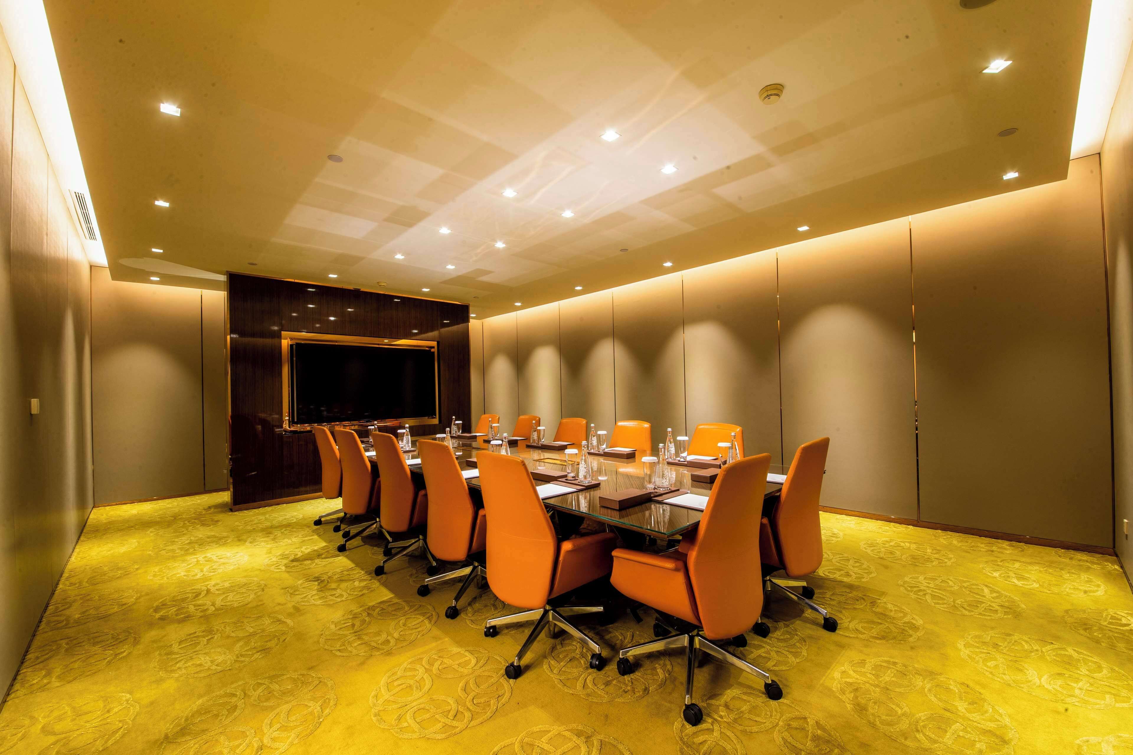 A conference room with a long table, multiple chairs, and a large screen.