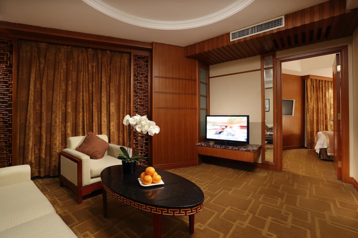 A hotel room with a sofa, a coffee table with fruit, a TV, and a traditional Asian-style wall.