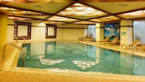 Una piscina interior con agua cristalina, vigas de madera en el techo y sillones de descanso a los lados.