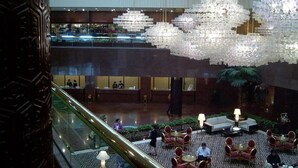 Un vestíbulo amplio con techo alto, un candelabro central y una zona de estar con mesas y sillas.