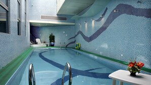 Une piscine intérieure à l’eau claire, un mur recouvert de carreaux avec un motif ondulé et une petite table sur laquelle est posé un vase de fleurs.