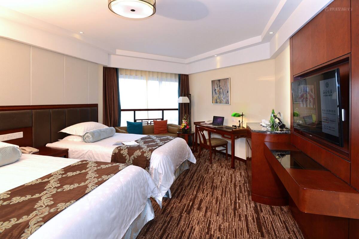 A hotel room with two beds, a desk, a TV, and a window with curtains.