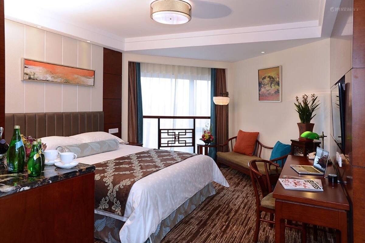 A hotel room with two beds, a desk with a laptop, a TV, and a dining area with chairs.