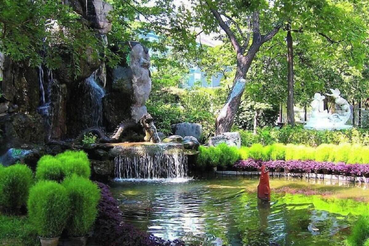 A serene garden with a pond, a waterfall, and a statue.