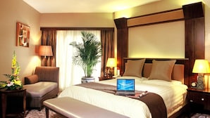 Une chambre d’hôtel avec un grand lit, un bureau, une chaise, une plante en pot et un ordinateur portable posé sur le lit.