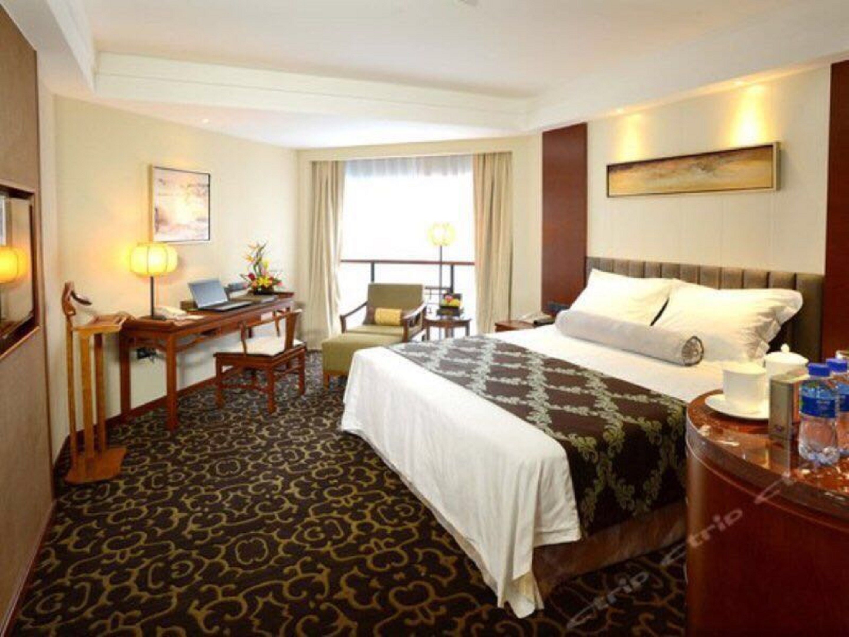 Una habitación de hotel con una cama, un escritorio con una computadora portátil, una silla, una ventana con cortinas y un cuadro en la pared.