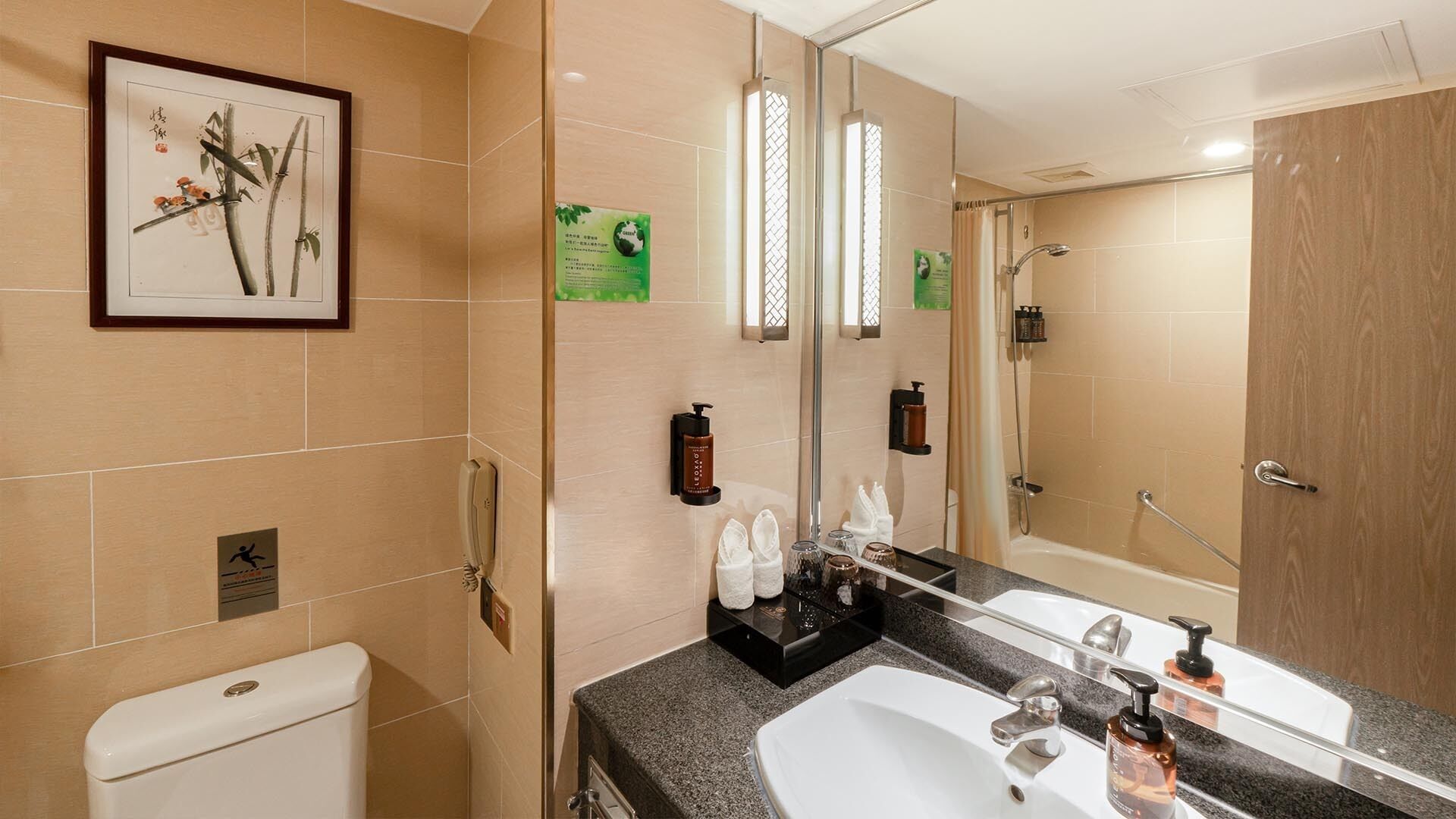 A modern bathroom with a toilet, sink, and shower. There is a framed artwork on the wall, a mirror, and various toiletries on the counter.