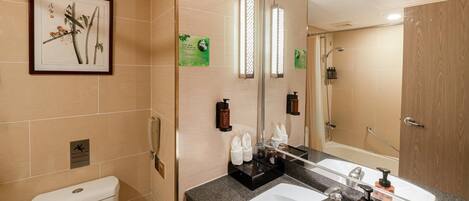 A modern bathroom with a toilet, sink, and shower. There is a framed artwork on the wall, a mirror, and various toiletries on the counter.