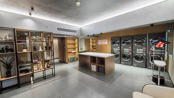 A modern laundry facility with multiple washing machines, a seating area, and a variety of decorative items on shelves.