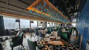 Un ristorante moderno con un pavimento a motivi geometrici, sedie verde e nere e un'installazione artistica a soffitto.