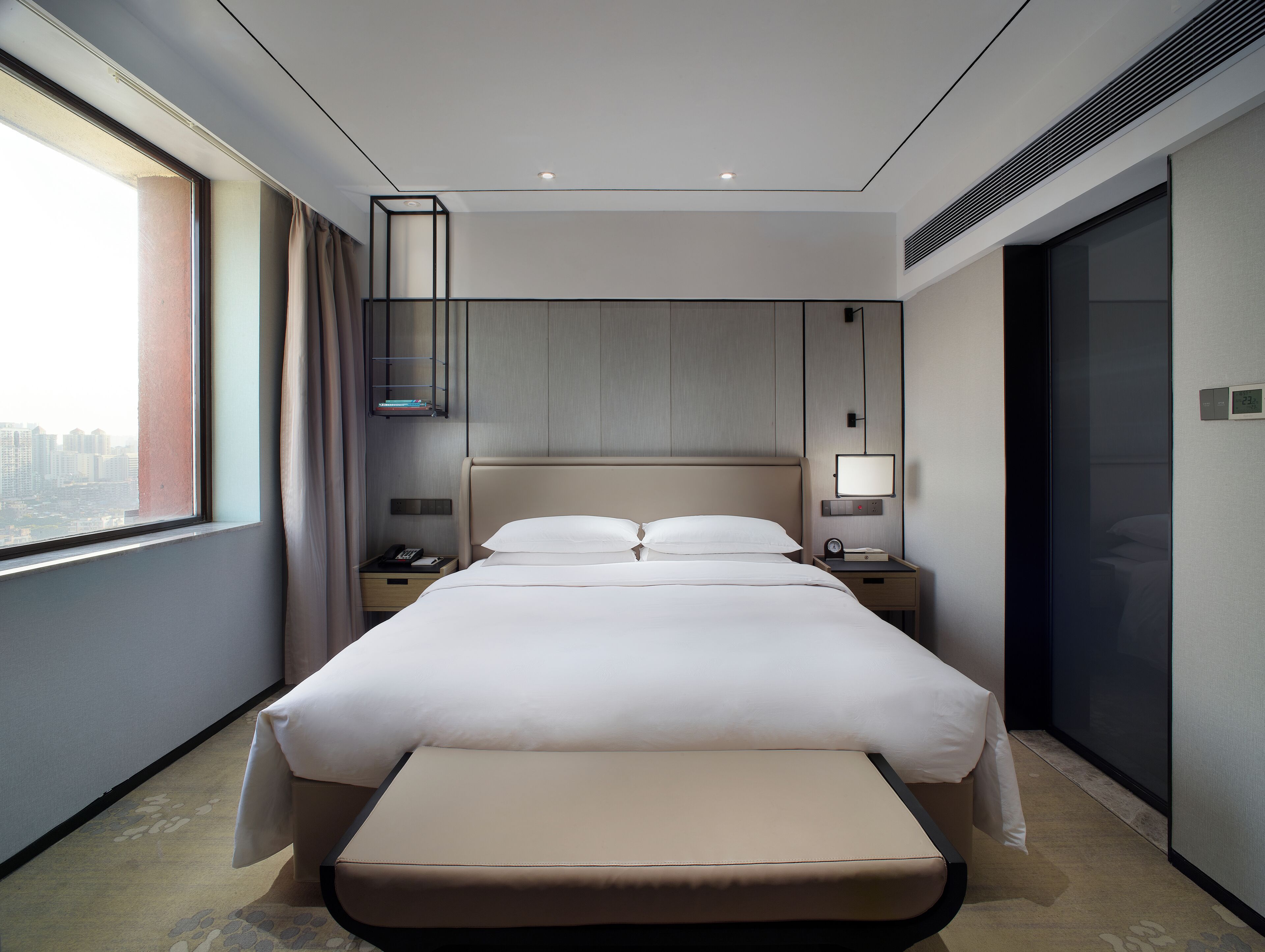 Ein modernes Hotelzimmer mit einem großen Bett, Nachttischen, Vorhängen vor einem Fenster und Blick auf die Stadt.