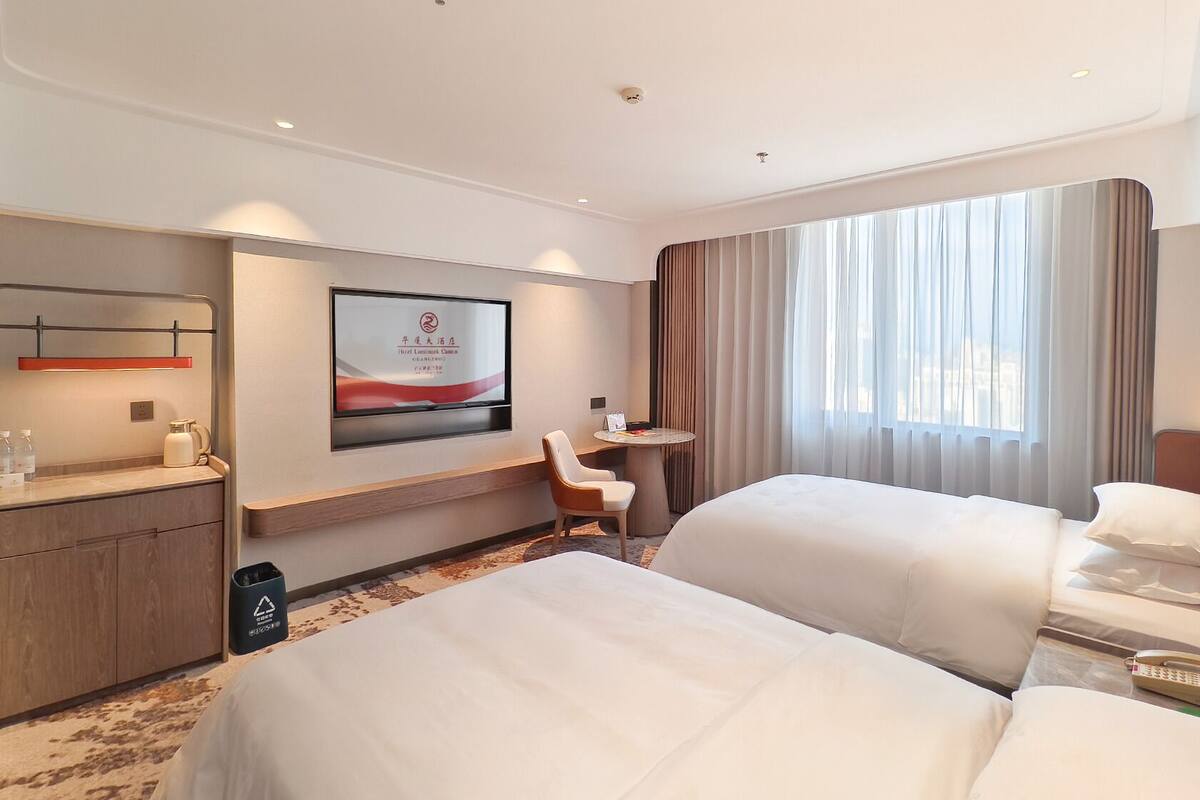 A hotel room with two beds, a desk, a chair, a TV, and a window with curtains.