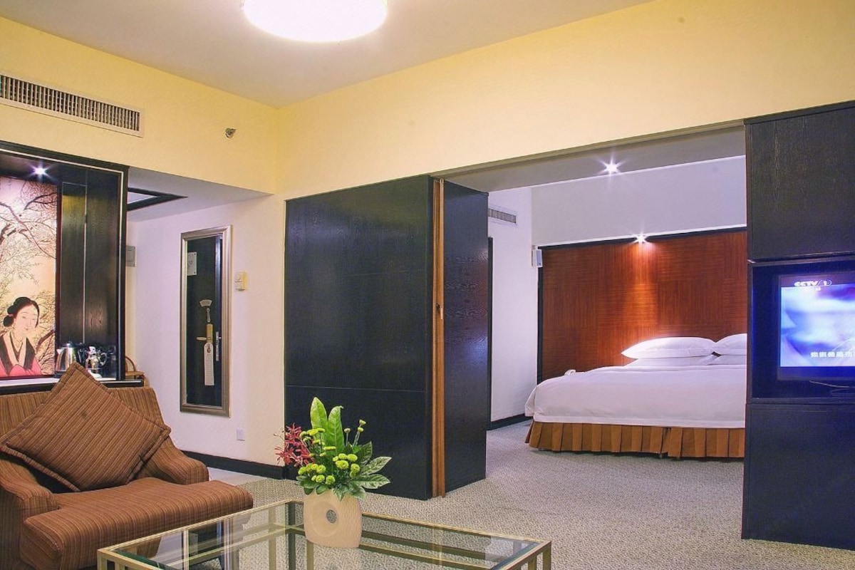 A hotel room with a bed, a television, a sofa, and a glass coffee table.
