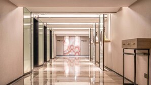 Un corridoio moderno di un hotel con porte in vetro, pavimento in marmo lucido e design minimalista.